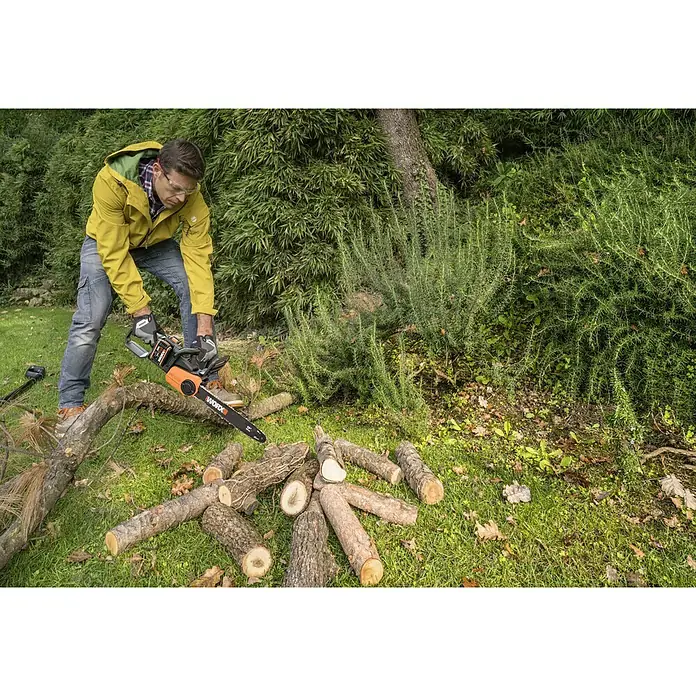 Worx PowerShare 20V Akku-Kettensäge WG384E - Akkuspannung: 40 V, Li-Ionen, 2 Ah, 2 Akkus, 35 cm - Ein Mann sägt mit einer Worx-Kettensäge Holz im Garten, wobei er Schutzbrille und Handschuhe trägt. Baumstämme liegen auf dem Rasen.