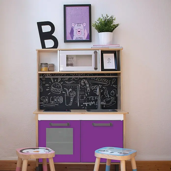 D-c-fix Klebefolie Uni Lack - 200 x 45 cm, Flieder, Selbstklebend - Foto einer Spielküche mit lila Schränken, einer Tafelrückwand und zwei kleinen Hockern davor, ideal für Kinder zum fantasievollen Spielen.