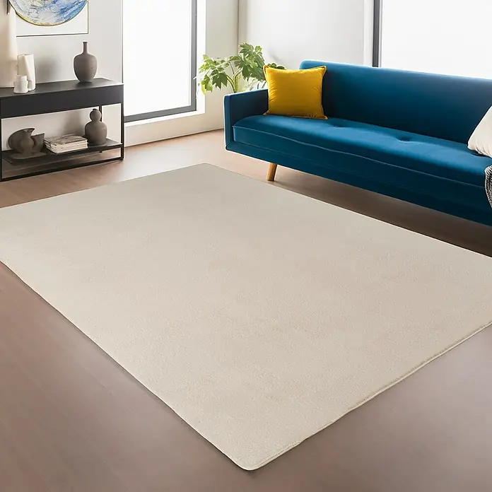 Kurzflorteppich Joy - Creme, 280 x 200 cm, 100 % Polyester - Ein beigefarbener Teppich liegt in einem Wohnzimmer mit blauem Sofa und schwarzen Regalen.