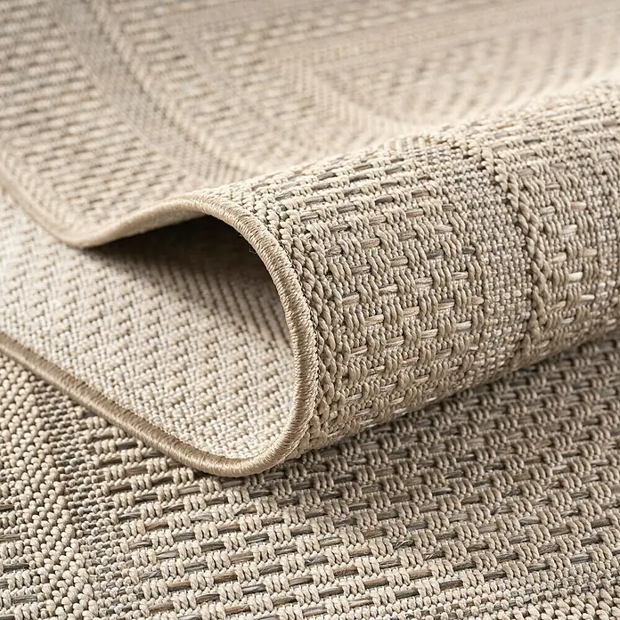 Outdoor-Teppich Desert 1304 - Beige, Durchmesser: 160 cm, 100 % Polypropylen - Detailaufnahme eines beigefarbenen Teppichs mit gewebter Textur, der aufgerollt ist und eine saubere, abgerundete Kante zeigt.