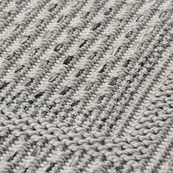 Outdoor-Teppich Desert 1304 - Grau, Durchmesser: 160 cm, 100 % Polypropylen - Detailaufnahme eines grauen, handgewebten Teppichs mit subtilen schwarzen Akzenten, die eine elegante Textur erzeugen.