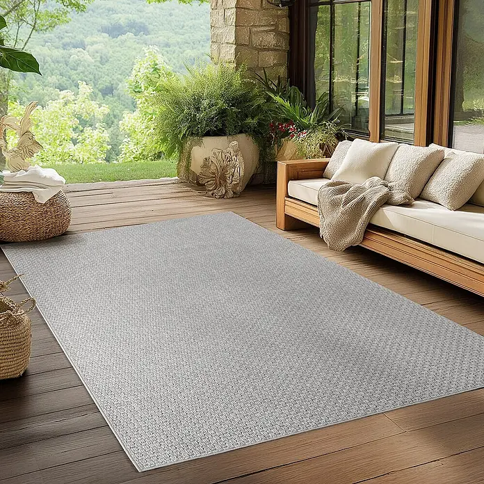 Outdoor-Teppich Ibiza II - Grau, 370 x 280 cm, 100 % Polypropylen - Ein grauer Outdoor-Teppich liegt auf einer Holzterrasse mit Möbeln und Pflanzen. Der Teppich hat eine feine Webstruktur.