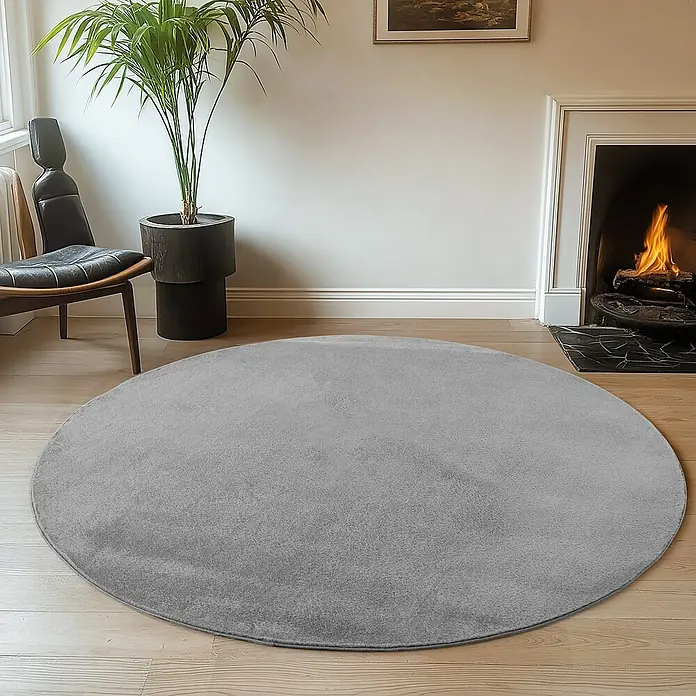 Kurzflorteppich Joy - Grau, Durchmesser: 80 cm, 100 % Polyester - Ein runder, grauer Teppich liegt in einem gemütlichen Wohnzimmer mit Kamin und Zimmerpflanze. Der weiche Teppich lädt zum Verweilen ein.