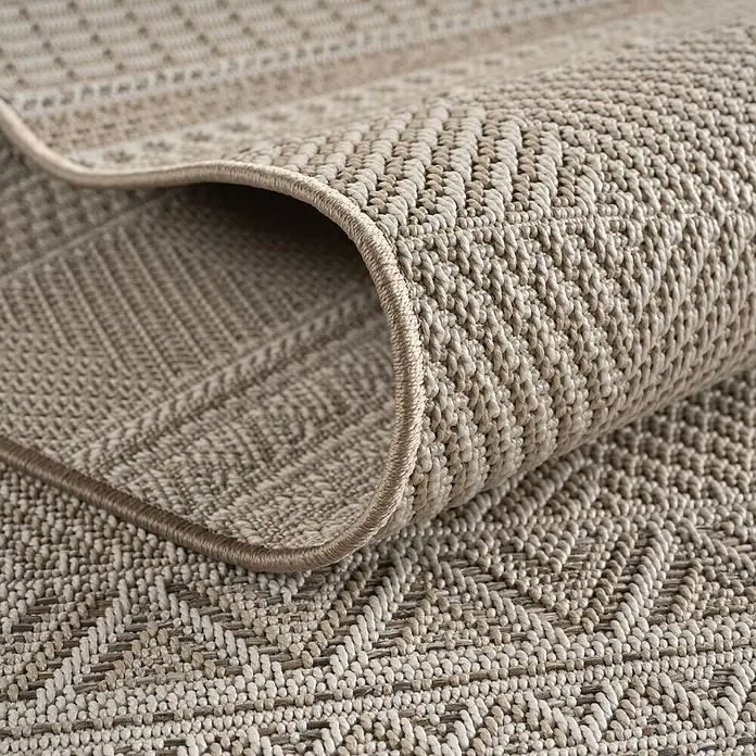 Outdoor-Teppich Desert 1302 - Beige, Durchmesser: 200 cm, 100 % Polypropylen - Detailaufnahme eines beigefarbenen Teppichs mit einem gewebten Zickzackmuster und gerollter Kante, der die Textur betont.