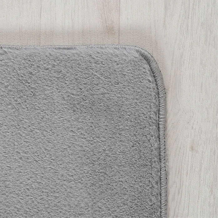 Kurzflorteppich Joy - Silber, 280 x 200 cm, 100 % Polyester - Nahaufnahme einer grauen Teppichkante auf hellem Holzboden, die die weiche Textur und die hochwertige Verarbeitung des Teppichs zeigt.