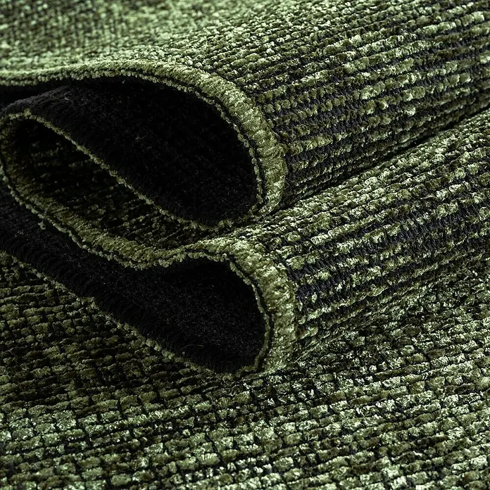 Flachgewebeteppich Space - Grün, 230 x 160 cm, 84 % Baumwolle, 16 % Polyester - Nahaufnahme eines gerollten olivgrünen Teppichs mit einer ausgeprägten Textur und einem dunklen, fast schwarzen Untergrund.