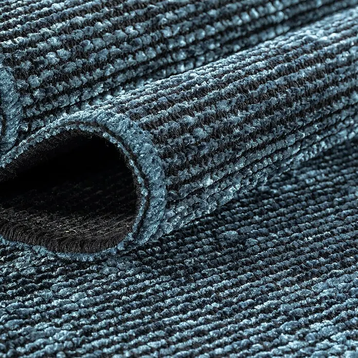 Flachgewebeteppich Space - Blau, 150 x 80 cm, 84 % Baumwolle, 16 % Polyester - Nahaufnahme eines gerollten Teppichs mit blau-schwarzem Streifenmuster, der eine weiche Textur und eine dunkle Unterseite zeigt.