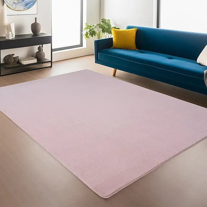 Kurzflorteppich Joy - Rosa, 280 x 200 cm, 100 % Polyester - Rosa Teppich in einem Wohnzimmer mit blauer Couch, Beistelltisch und Pflanzen. Der Teppich ist der zentrale Fokus.
