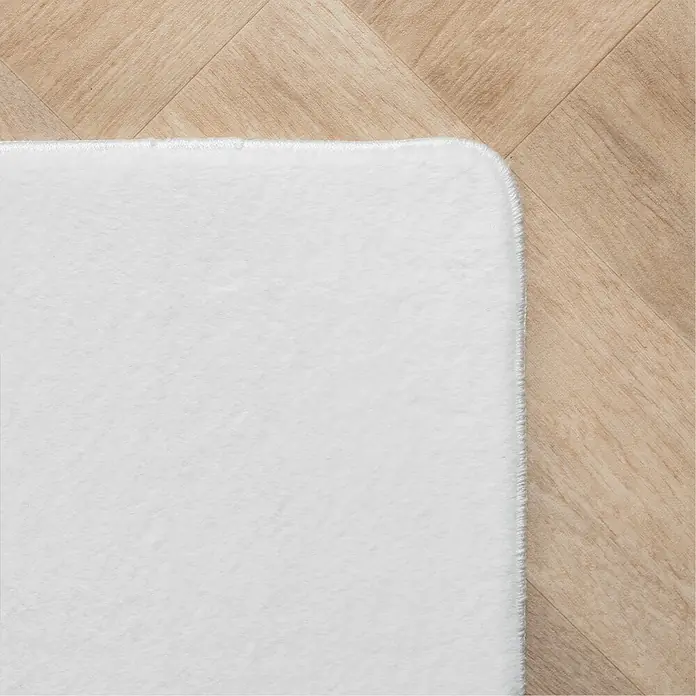 Kurzflorteppich Joy - Weiß, 100 x 60 cm, 100 % Polyester - Nahaufnahme eines weißen Teppichs mit weicher Textur auf einem hellen Holzboden, der Komfort und Wärme ausstrahlt.
