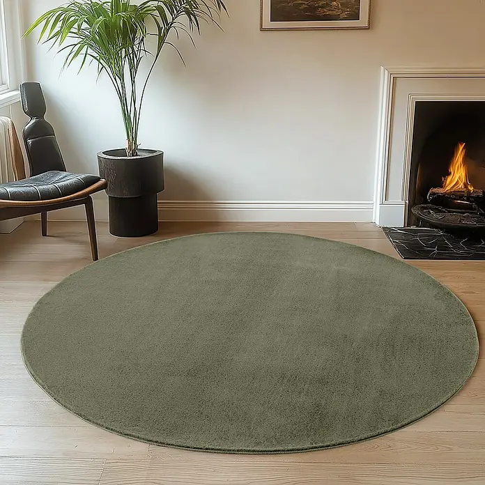 Kurzflorteppich Joy - Grün, Durchmesser: 200 cm, 100 % Polyester - Ein runder, olivgrüner Teppich liegt auf einem Holzboden in einem stilvollen Wohnzimmer.