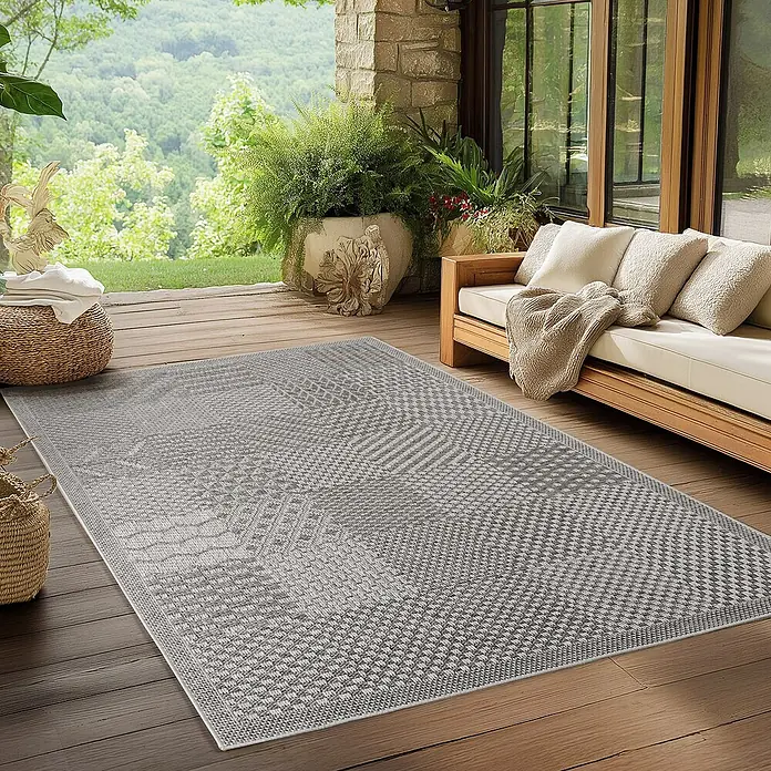 Outdoor-Teppich Ibiza I - Grau, 170 x 120 cm, 100 % Polypropylen - Ein grauer Outdoor-Teppich mit geometrischem Muster liegt auf einer Holzterrasse neben einem Sofa.