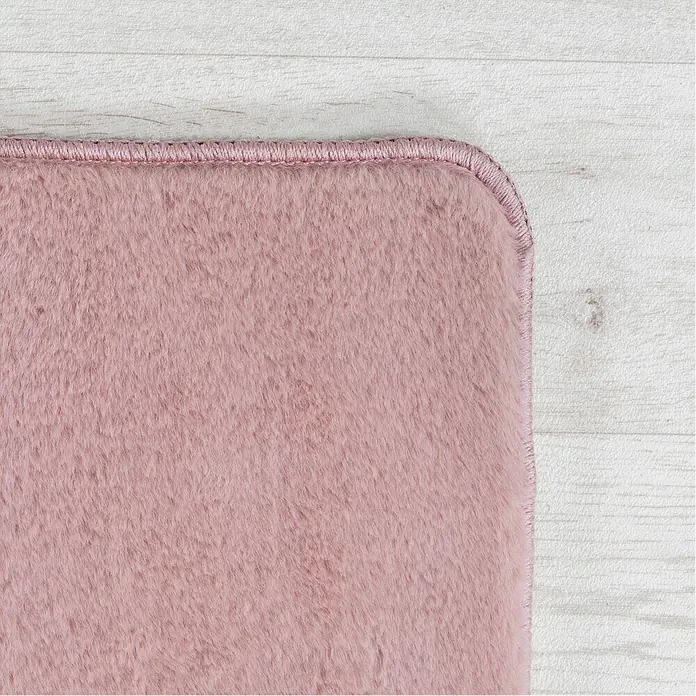 Kurzflorteppich Joy - Rosa, 100 x 60 cm, 100 % Polyester - Nahaufnahme eines rosafarbenen, flauschigen Teppichs mit passendem Rand, der auf einem hellen Holzboden liegt.