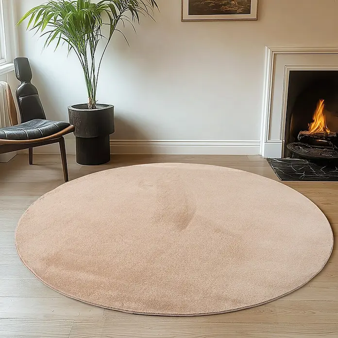 Kurzflorteppich Joy - Beige, Durchmesser: 200 cm, 100 % Polyester - Ein runder, beiger Teppich liegt auf einem Holzboden, der Wärme und Komfort in einem gemütlichen Wohnraum ausstrahlt.