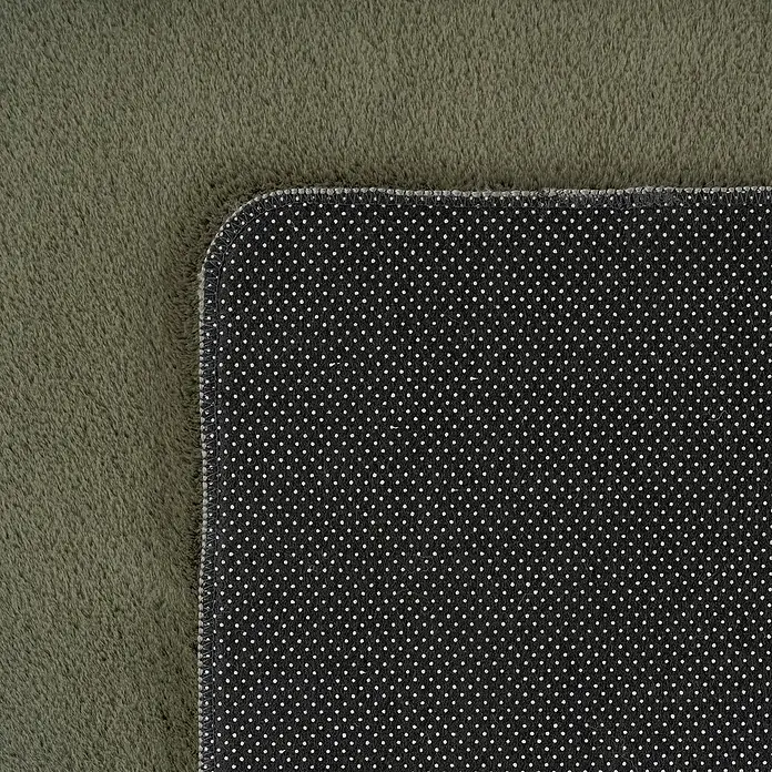 Kurzflorteppich Joy - Grün, 280 x 200 cm, 100 % Polyester - Nahaufnahme eines Teppichs mit olivgrünem Flor und schwarzer Unterseite mit weißen Punkten.