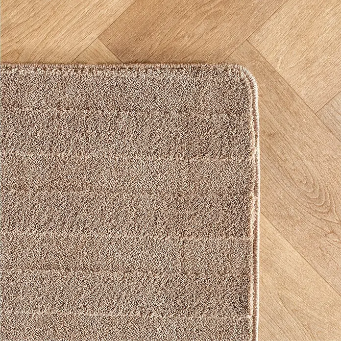 Kurzflorteppich Pompei 1611 - Beige, 150 x 80 cm, 100 % Polyester - Nahaufnahme einer beigefarbenen Badematte mit dezenten Streifen auf einem hellen Holzboden mit Fischgrätmuster.