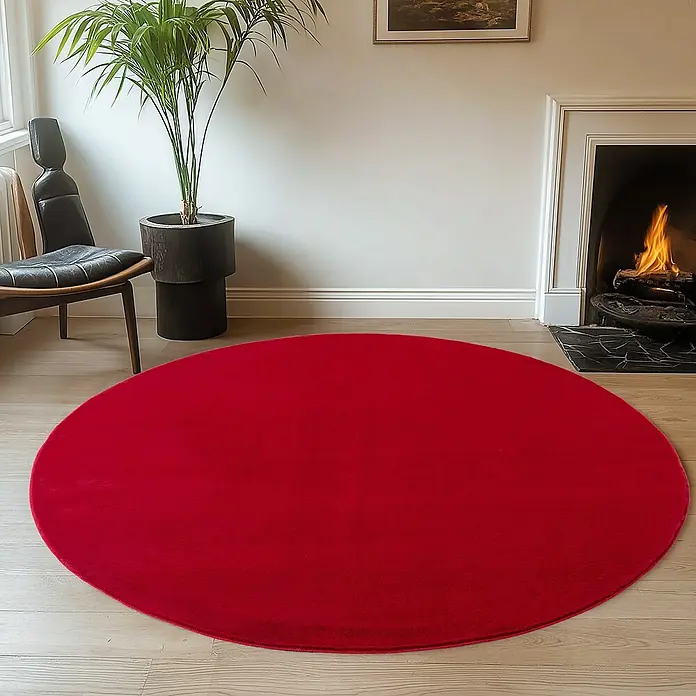 Kurzflorteppich Joy - Rot, Durchmesser: 160 cm, 100 % Polyester - Ein roter runder Teppich liegt in einem gemütlichen Wohnzimmer mit Kamin, Sessel und Zimmerpflanze.