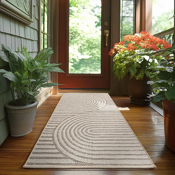 Outdoor-Teppich Desert 1301 - Beige, 150 x 80 cm, 100 % Polypropylen - Ein beigefarbener Läufer mit einem modernen Halbkreis-Muster liegt auf einem Holzboden, umgeben von Pflanzen und einer Tür.