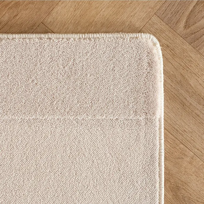 Kurzflorteppich Pompei 1614 - Creme, 230 x 160 cm, 100 % Polyester - Nahaufnahme eines beigefarbenen Badteppichs mit schlichter Bordüre auf einem Holzboden.