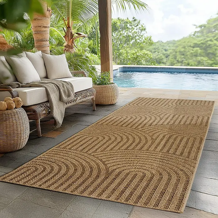 Outdoor-Teppich Timber 1401 - Beige, 150 x 80 cm, 100 % Polypropylen - Ein dekorativer brauner Outdoor-Teppich mit einem geometrischen Muster liegt auf einer Terrasse neben einem Pool und einer Sitzgruppe.