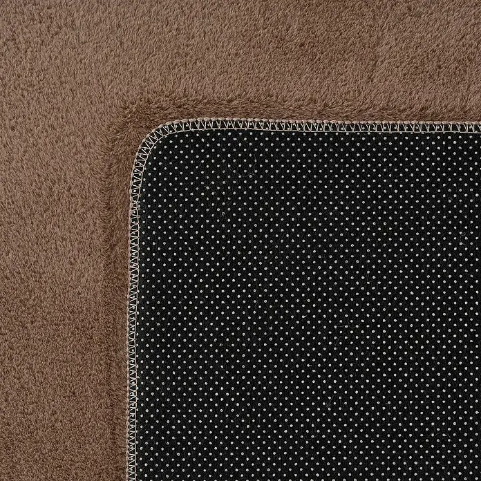 Kurzflorteppich Joy - Mokka, 100 x 60 cm, 100 % Polyester - Detailaufnahme eines braunen Teppichs mit einer schwarzen, gepunkteten Unterseite, die die Textur und Verarbeitung hervorhebt.
