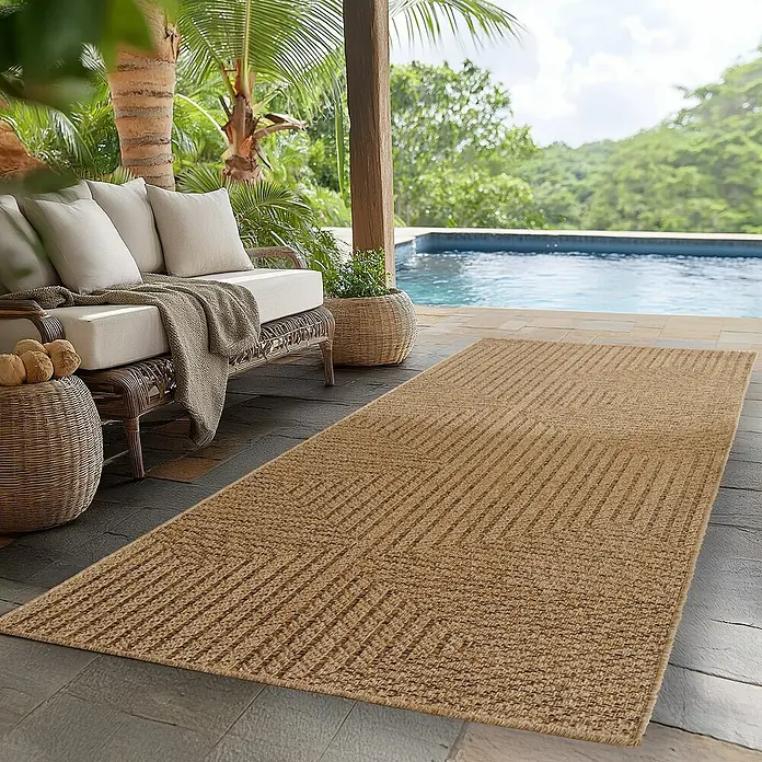 Outdoor-Teppich Timber 1404 - Beige, 150 x 80 cm, 100 % Polypropylen - Ein beigefarbener Outdoor-Teppich mit einem geometrischen Zickzackmuster liegt auf einer Terrasse neben einem Rattan-Sofa und einem Pool.