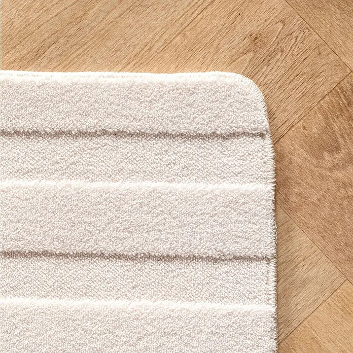 Kurzflorteppich Pompei 1611 - Creme, 150 x 80 cm, 100 % Polyester - Ein cremefarbener Badteppich mit strukturierten Streifen liegt auf einem hellen Holzboden. Die weiche Textur lädt zum Barfußlaufen ein.