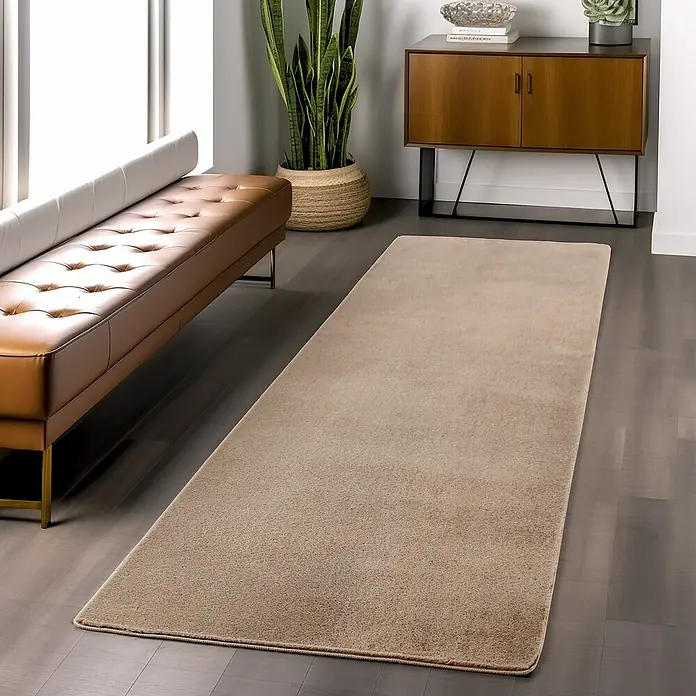 Kurzflorteppich Joy - Beige, 100 x 60 cm, 100 % Polyester - Ein beigefarbener Teppich liegt in einem modernen Wohnzimmer zwischen einem Ledersofa und einem Holzschrank.