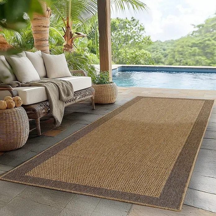 Outdoor-Teppich Timber 1402 - Beige, 250 x 80 cm, 100 % Polypropylen - Ein rechteckiger, hellbrauner Teppich mit dunklerem Rand auf einer Terrasse neben einem Pool und einer Sitzecke.
