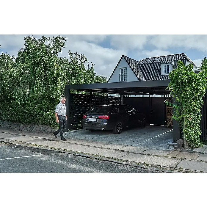 Carport Cubus - Außenmaß inkl. Dachüberstand (B x T): 5,8 x 5,5 m, Doppelcarport, Grau - Ein stilvolles, schwarzes Auto parkt unter einem modernen Carport vor einem Haus mit dunklem Dach und einem Mann, der vorbeigeht.