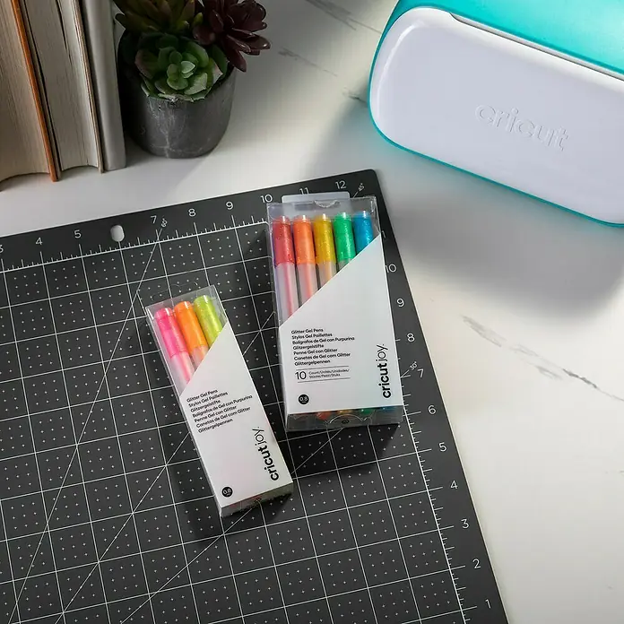 Cricut Joy Gelroller-Set Glitzergelstifte - 10 -tlg., Mehrfarbig, Strichstärke: 0,8 mm, Glitzernd - Nahaufnahme von zwei Cricut Joy Glitter Gel Pens Sets auf einem Schneidebrett, ideal für Bastelprojekte.