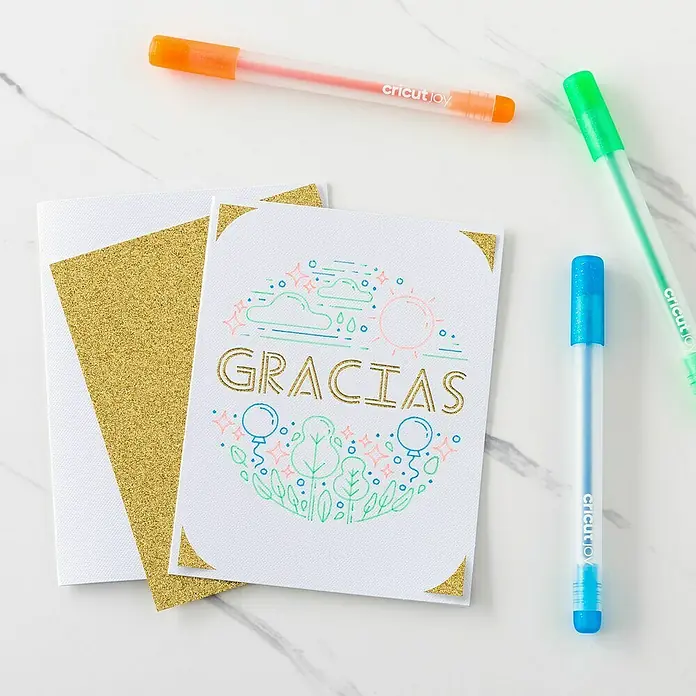 Cricut Joy Gelroller-Set Glitzergelstifte - 10 -tlg., Mehrfarbig, Strichstärke: 0,8 mm, Glitzernd - Cricut Joy Stifte in Orange, Grün und Blau neben einer Grußkarte mit der Aufschrift "Gracias" und goldenem Glitzerakzenten.