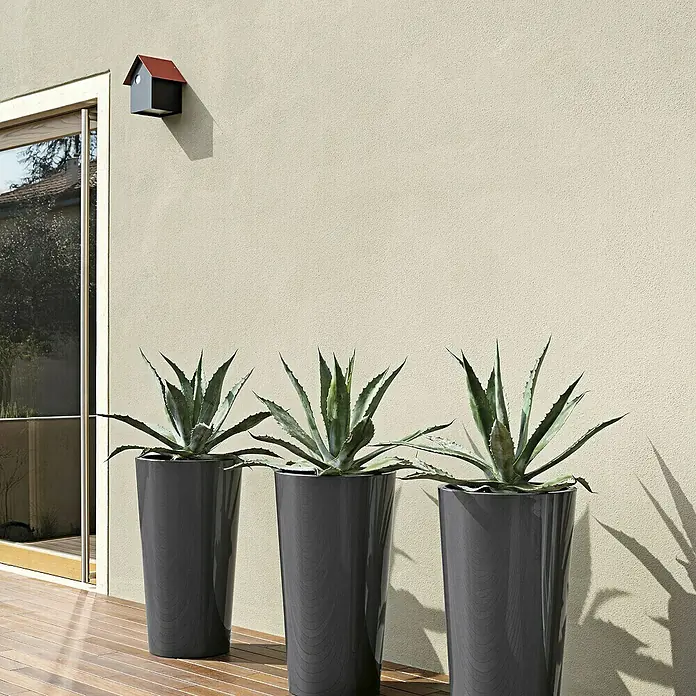 Euro3plast Pflanzsäule rund Tuit - Außenmaß (Ø x H): 33 x 61 cm, Kunststoff, Anthrazit Glänzend - Drei schlanke, graue Pflanzgefäße mit Agaven auf einer Holzterrasse vor einer hellen Wand mit einem kleinen Vogelhaus.