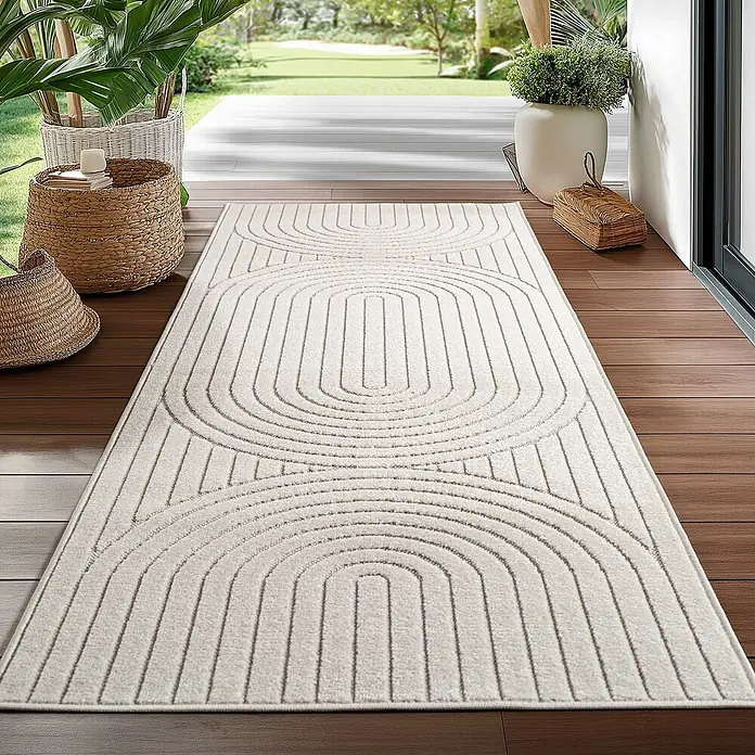 Outdoor-Teppich Nova I - Creme, 250 x 80 cm, 100 % Polypropylen - Ein cremefarbener Teppich mit einem modernen, geometrischen Design liegt auf einer Holzterrasse und sorgt für einen stilvollen Übergang nach draußen.