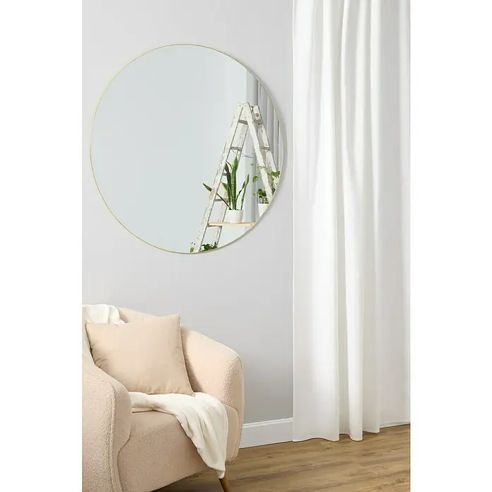 Espejo de pared Napoli - Diámetro: 100 cm, Dorado - Un interior elegante con un espejo redondo que refleja una escalera, un sillón cómodo y cortinas elegantes.