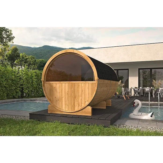 Tuindeco Fasssauna - L x B x H: 350 x 205 x 220 cm, Ohne Ofen, ½‑Panorama‑Fenster - Holzfass-Sauna neben Pool mit Schwanen-Luftmatratze. Die Fasssauna ist aus hellem Holz gefertigt und hat ein Dach aus dunklen Schindeln.