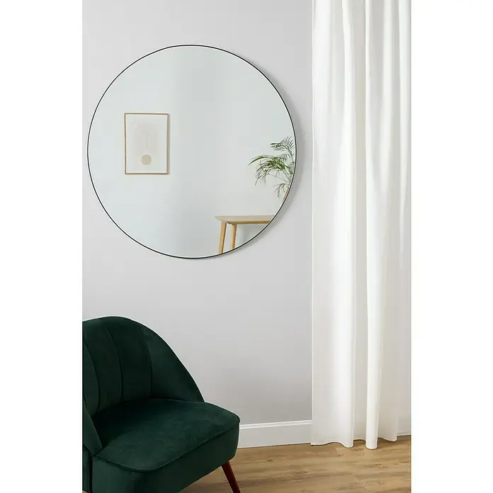 Espejo de pared Napoli - Diámetro: 100 cm, Negro - Un gran espejo redondo con marco negro cuelga de una pared blanca, junto a un sillón de terciopelo verde y una cortina blanca.