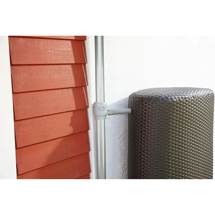 Garantia Füllautomat Mini - Grau, Passend für: Fallrohre von DN 50 - 60 - Regenwasserbehälter aus Rattan neben einem Fallrohr an einer Hauswand. Ideal für die Gartenbewässerung und umweltfreundliche Wassernutzung.