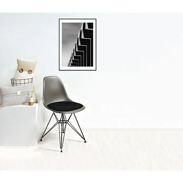 Nielsen Alurahmen Pixel - 50 x 50 cm, Schwarz - Ein grauer Stuhl mit schwarzem Sitzkissen steht vor einer Wand, an der ein gerahmtes Bild hängt, und bietet eine stilvolle und komfortable Sitzgelegenheit.
