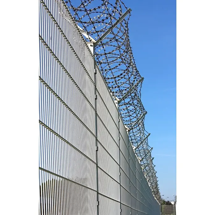 Mattenzaun Vega 2D - Feuerverzinkt, B x H: 2.500 x 830 mm, Stahl - Bild einer hohen Sicherheitszaunanlage mit Stacheldraht gegen einen blauen Himmel. Der Zaun ist hellgrau und besteht aus vertikalen Streben.