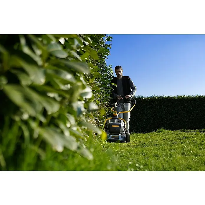 Stiga Akku-Rasenmäher Combi 753E V KIT - 48 V, 2 Akkus, 5 Ah, Schnittbreite: 51 cm - Mann mäht Rasen mit einem STIGA Rasenmäher entlang einer Hecke, blauer Himmel im Hintergrund.