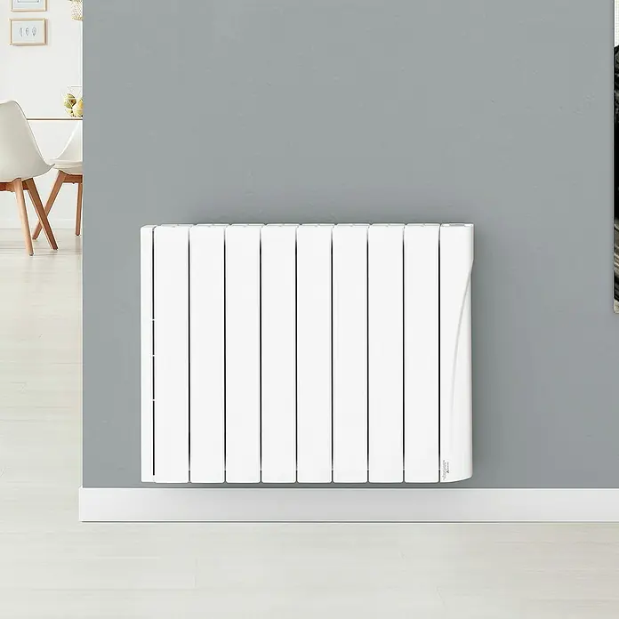 Voltomat Emisor térmico WiFi I - 1.250 W, Blanco, 9,5 x 74 x 57,5 cm, Cerámico - Un radiador blanco está montado en una pared gris. Cuenta con varios paneles verticales y un acabado elegante y moderno.