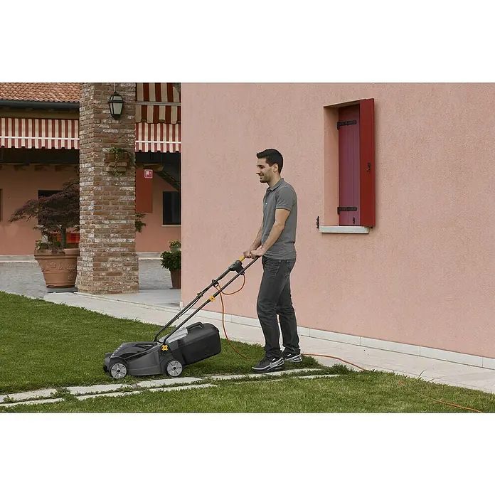 Alpina Elektro-Rasenmäher BL 320 E - 1.000 W, Schnittbreite: 32 cm - Ein Mann mäht mit einem grauen Rasenmäher der Marke unbekannt den Rasen. Das Gerät verfügt über einen Fangkorb und gelbe Akzente.