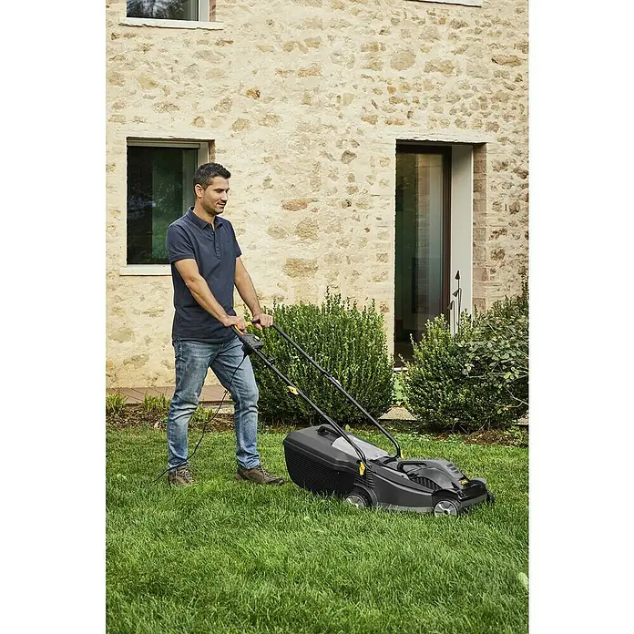 Alpina Elektro-Rasenmäher BL 380 E - 1.400 W, Schnittbreite: 38 cm - Ein Mann mäht den Rasen mit einem schwarzen Rasenmäher auf einer grünen Wiese. Ein Haus ist im Hintergrund zu sehen.