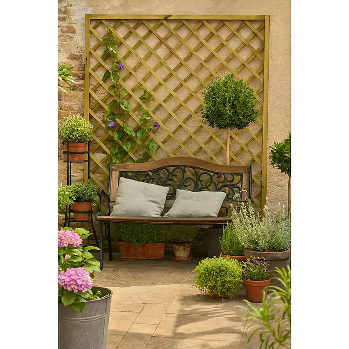 Cerland Celosía para exterior Premices - 180 x 180 cm, Madera, Natural - Banco de jardín con cojines frente a un enrejado de madera, rodeado de plantas en macetas que crean un rincón de jardín tranquilo.