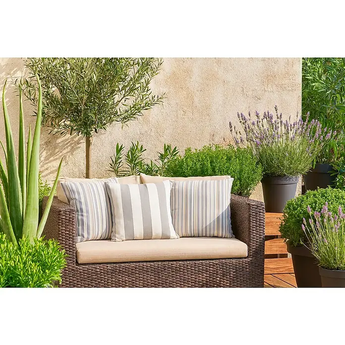Cojín Deco Rayas - 50 x 50 cm, Plástico, Gris - Acogedor sofá de exterior con cojines a rayas, ubicado entre exuberante vegetación y plantas de lavanda, ideal para momentos de relax en el jardín.