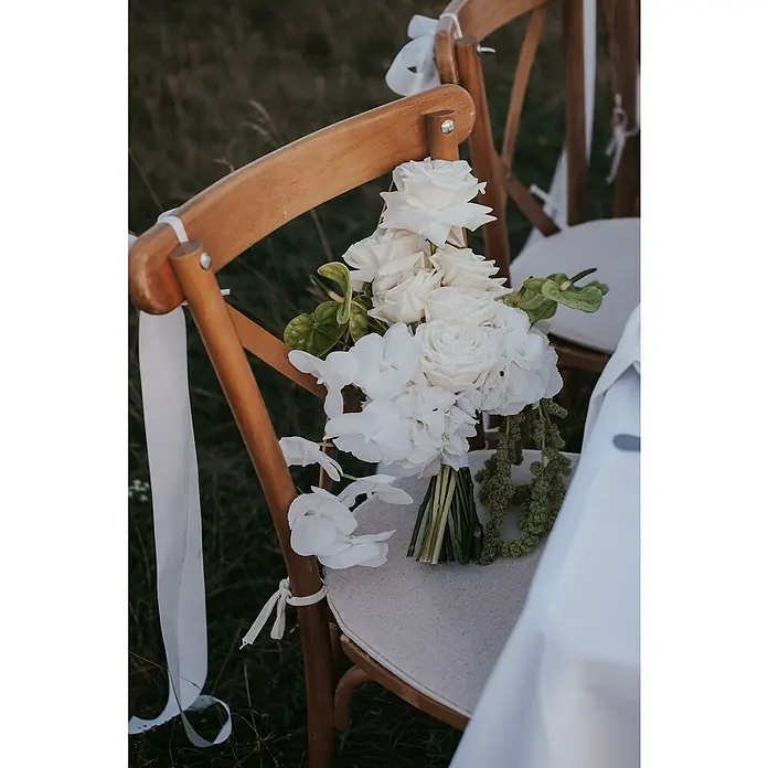 Stapelstuhl Crossback - 1 Stk., Ulmenholz, Braun, B x T x H: 48 x 47 x 89 cm - Ein rustikaler Holzstuhl mit einem eleganten, weißen Blumenstrauß und zarten Schleifen für eine Hochzeitszeremonie im Freien.