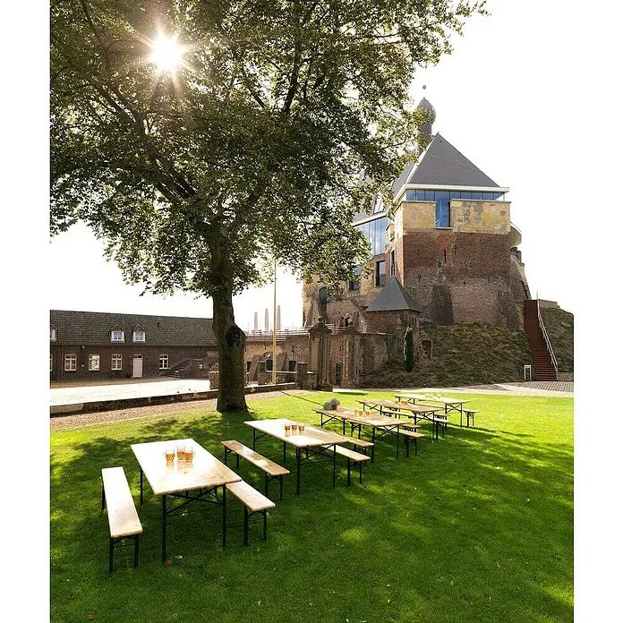 Feros Biertisch - L x B x H: 220 x 50 x 78 cm, Stahl, Kiefer, Rechteckig, Braun/Schwarz - Biertische und -bänke auf Rasen vor historischer Burg. Ideal für Feste im Freien, mit Biergläsern auf den Tischen.