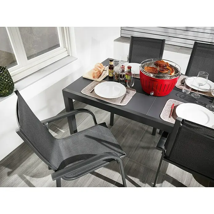 Sunfun Maja Gartenmöbel-Set I - 5 -tlg., Glas/Textilen, Anthrazit - Tischgedeck mit Grill und Speisen. Der Grill ist rot und es liegen Fleischstücke darauf. Die Teller sind weiß und es gibt Getränke.