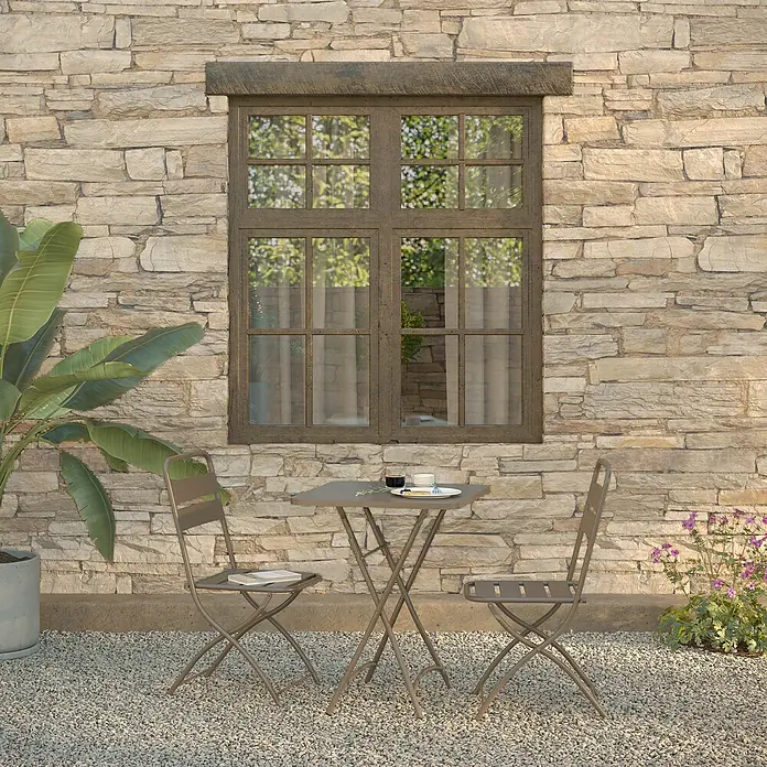 Feros Balkonmöbel-Set Breeze - 3 -tlg., Metall, Braun - Eine Nahaufnahme eines Bistro-Sets mit Tisch und zwei Stühlen vor einer rustikalen Steinmauer mit Fenster.