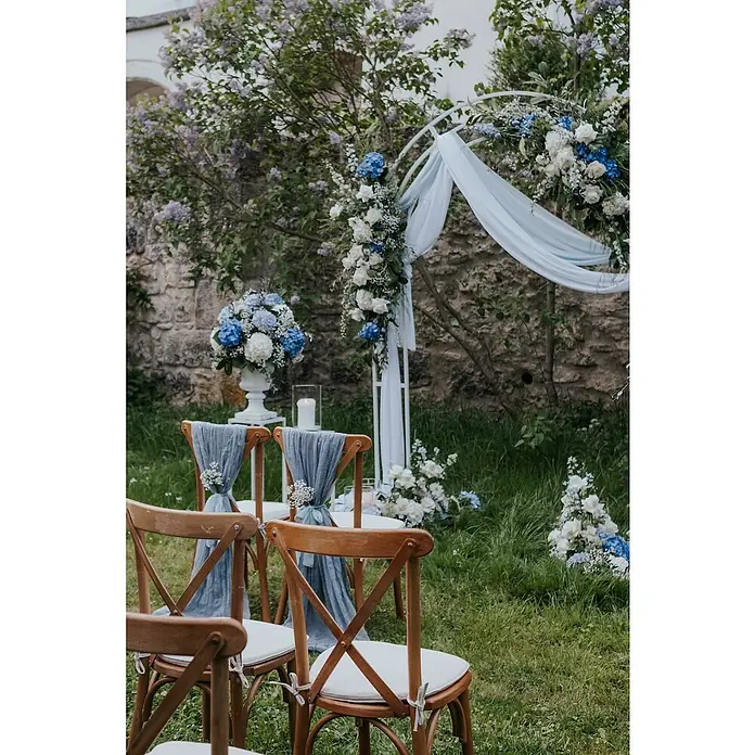 Stapelstuhl Crossback - 1 Stk., Ulmenholz, Braun, B x T x H: 48 x 47 x 89 cm - Ein romantisches Hochzeitsarrangement mit Stühlen, blauem Tuch und Blumen unter einem dekorativen Bogen.